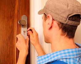 Persona con gorra abre puerta de madera con una llave.