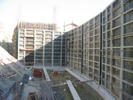 Cantiere edile con impalcature in metallo e pozza d'acqua sul fondo.