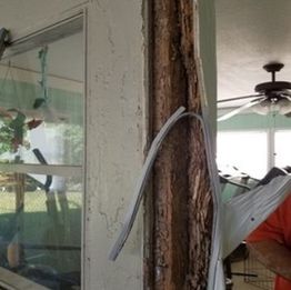 Worn door frame with exposed wood and wire inside a room with a ceiling fan.