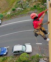 Persona escalando edificio con casco rojo mientras vehículos pasan abajo.