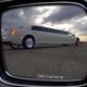 Limousine reflection in side mirror under cloudy sky.