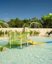 Piscina infantil con juegos de agua y tobogán bajo un cielo azul claro.