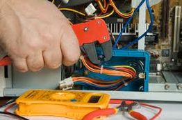 Hand using tools to repair computer wires; multimeter and pliers visible.