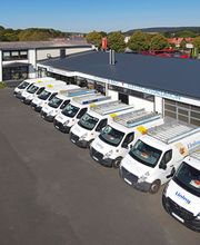 Reihe von weißen Transportern vor einem Gebäude mit Büro- und Garagenbereich.