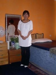 Eine Person in weißem Oberteil steht in einem orange gestrichenen Zimmer neben einem Bett.