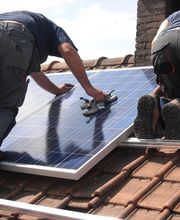 Personas instalando paneles solares en el tejado de una casa bajo un cielo despejado.