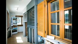 Interno luminoso con finestre in legno e persiane, espositori di prodotti a lato.