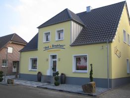 Gelbes Gebäude mit der Aufschrift "Bed & Breakfast" und dekorativen Pflanzen am Eingang.