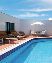 Piscina em terraço com espreguiçadeiras de madeira e guarda-sol branco. Céu azul ao fundo.