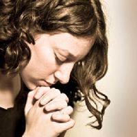 Woman with curly hair praying with hands clasped.