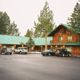 Rustic lodge with green roofs, surrounded by trees and cars parked in front.