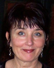 Eine lächelnde Frau mit kurzen, dunklen Haaren und Ohrringen vor dunklem Hintergrund.