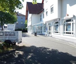Ein Immobilienbüro mit Anhänger auf einer gepflasterten Straße bei sonnigem Wetter.