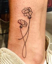 Tatoeage van twee eenvoudige bloemen op het onderbeen. Schoenen op de achtergrond.