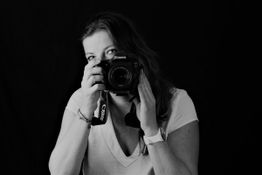 Frau mit Kamera macht ein Foto, schwarzer Hintergrund, Schwarz-Weiß-Bild.