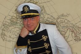 Ein Mann in Uniform mit Mütze posiert vor einer antiken Weltkarte.