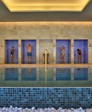 Personas duchándose en cabinas azules frente a una piscina techada.