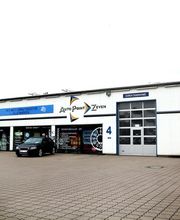 Mehrere Autos vor einer Autowerkstatt mit Glasgaragentoren und einem großen Firmenlogo.