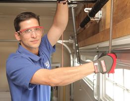 Man in safety glasses and gloves adjusting a garage door mechanism.