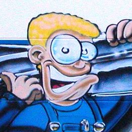 Comicfigur mit blonden Haaren und großer Brille in blauer Latzhose zeigt Daumen hoch.