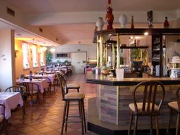 Gemütliches Restaurant mit Holzstühlen, gedeckten Tischen und einer Bar im Vordergrund.