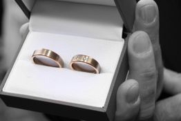 Zwei Eheringe in einer Schachtel werden in der Hand gehalten. Einer hat kleine Diamanten.