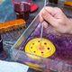 Hand creating marbling art with tool in tray of colorful ink and water.