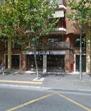 Fachada de un edificio con árboles y una persona caminando en la acera.