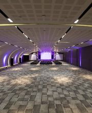Sala de conferencias vacía con iluminación púrpura y techo curvado. Suelo de moqueta gris.