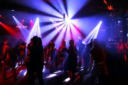 Menschen tanzen in einem Club, umgeben von bunten Lichtern und einer lebhaften Atmosphäre.