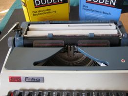 Schreibmaschine mit zwei Duden-Büchern im Hintergrund: Rechtschreibung und Fremdwörter.