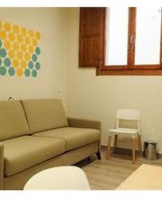Sala con sofá beige, silla, ventana y decoración geométrica en la pared.