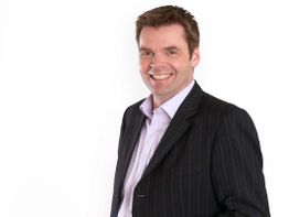 Ein lächelnder Mann im Anzug vor weißem Hintergrund.