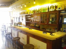 Gemütliche Bar mit Holztresen, Barhockern und vielen Flaschen im Regal, warm beleuchtet.