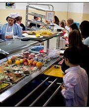 Schulkantine mit Schülern in der Essensausgabe, Tabletts und frische Lebensmittel auf der Theke.
