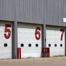 Garage doors numbered 5, 6, and 7 in red on a metal building.