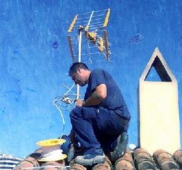 Persona instalando una antena parabólica en un tejado bajo un cielo azul.