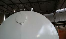 Tanque industrial branco em galpão, com tampa e tubulação visíveis na parte superior.