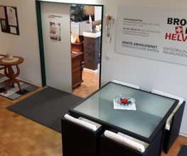 Eingangsbereich eines Brockenhauses mit Tischgruppe und Informationsschild an der Wand.