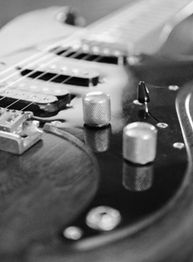 Nahaufnahme einer elektrischen Gitarre in Schwarz-Weiß mit Fokus auf Reglerknöpfe und Saiten.