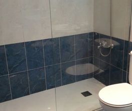 Baño moderno con ducha de vidrio, inodoro y bidé sobre baldosas azules y blancas.