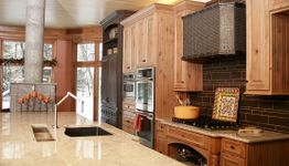 Rustic kitchen with wooden cabinets, granite island, and modern appliances, overlooking snowy trees.