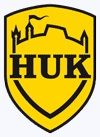 Gelbes Wappen mit schwarzem Text "HUK" und stilisiertem Burgturm.
