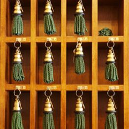 Wooden key holder with rows of hooks and keys, each with green tassels hanging down.