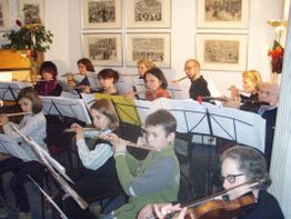 Eine Gruppe von Musikern spielt Flöten und Geige in einem Raum mit gerahmten Bildern an der Wand.