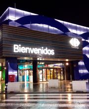 Entrada iluminada de Carrefour con cartel de "Bienvenidos" bajo la lluvia nocturna.
