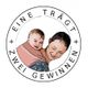 Eine Frau trägt ein lächelndes Baby im Tragetuch. Text: "EINE TRÄGT, ZWEI GEWINNEN".