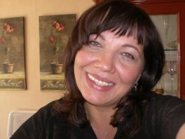 Eine lächelnde Frau vor Bildern mit Blumenmotiven an einer cremefarbenen Wand.