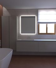 Bagno moderno con vasca, specchio retroilluminato e finestra con tenda chiusa.