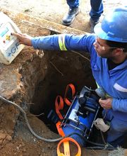 Trabalhador de capacete azul utiliza equipamento em buraco de construção.